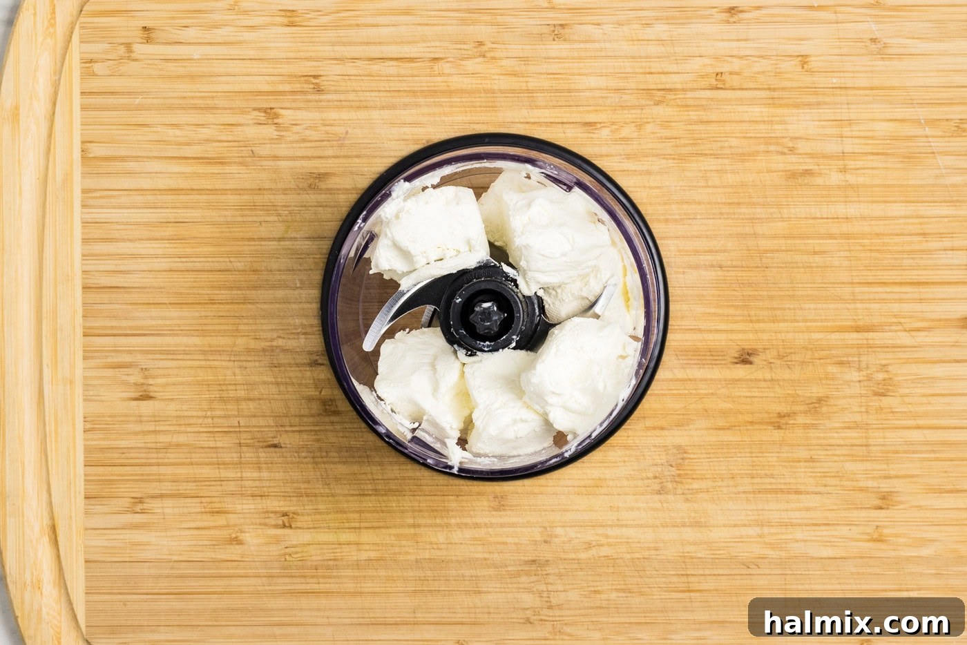 Cubed cream cheese resting in the bowl of a mini food chopper, ready for blending.