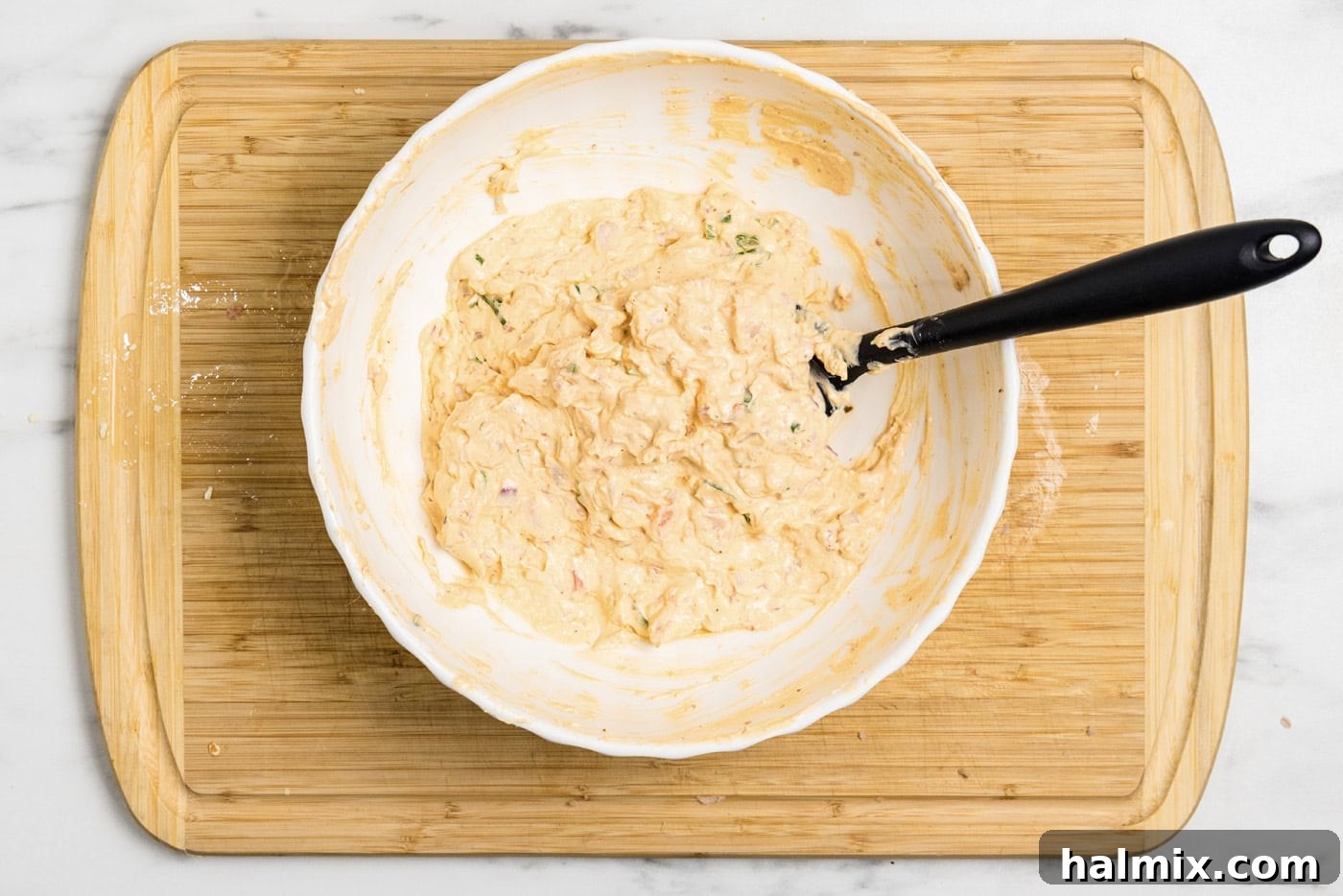 A rubber spatula resting in a bowl of freshly mixed shrimp dip, ready to be chilled.