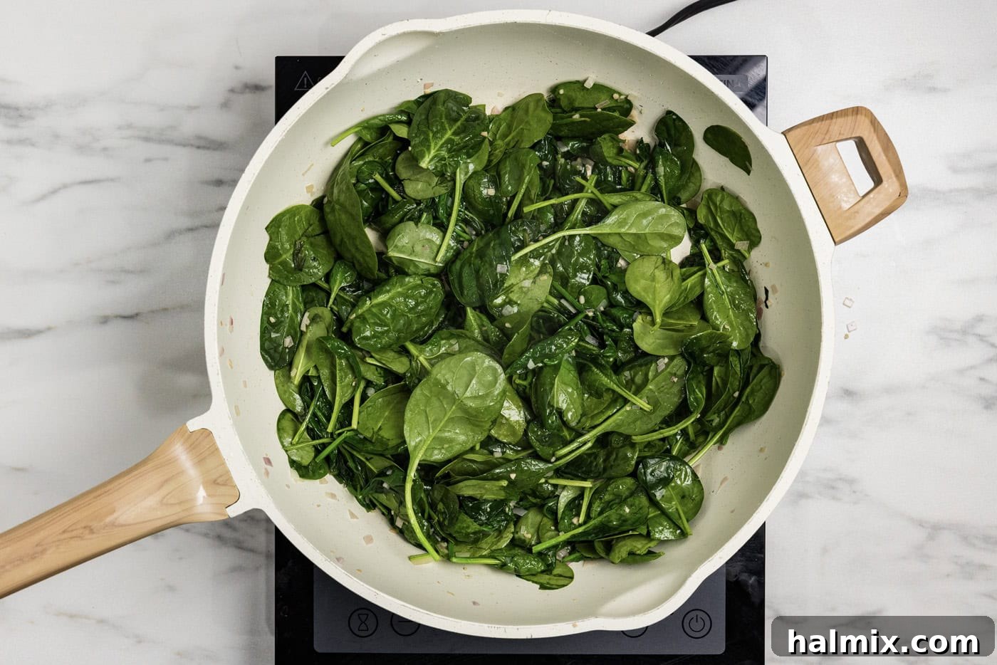 spinach leaves added to skillet with butter, garlic, and shallots, showing initial wilting
