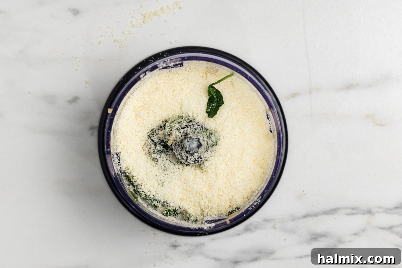 parmesan cheese added to spinach mixture in a food chopper, preparing for blending