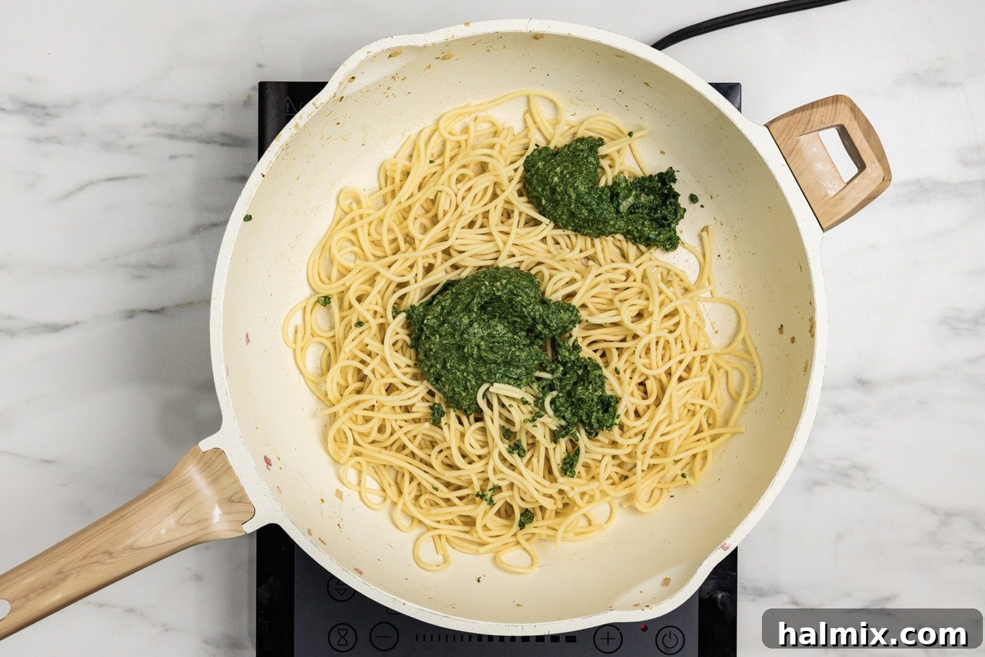 spinach sauce added to skillet with cooked spaghetti noodles, ready to be combined