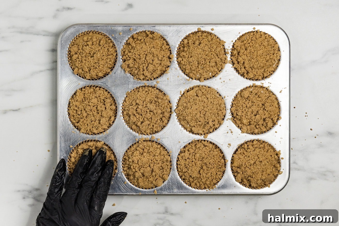 hand pressing down on streusel topping on top of muffin batter