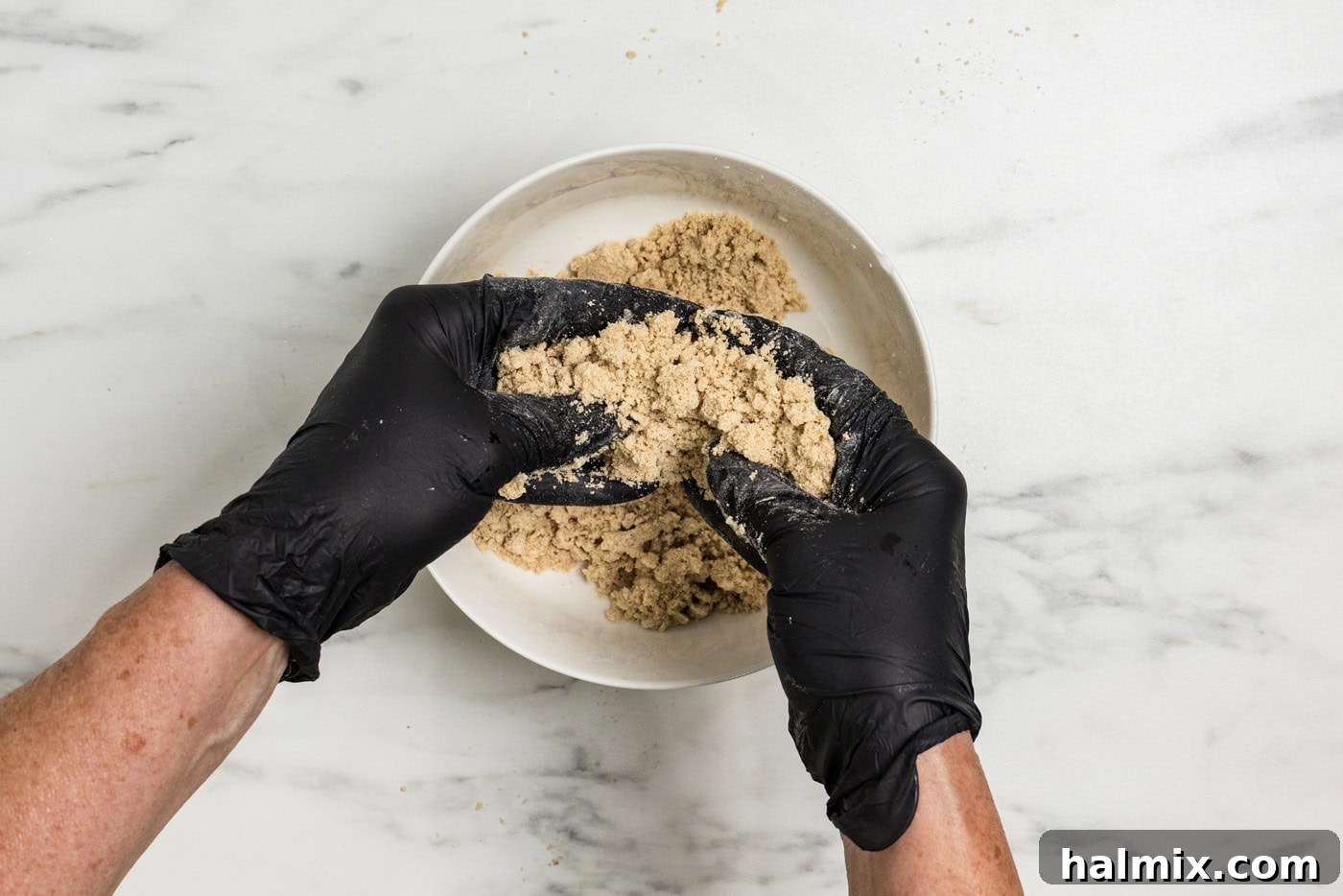 gloved hands squeezing streusel ingredients together in a bowl
