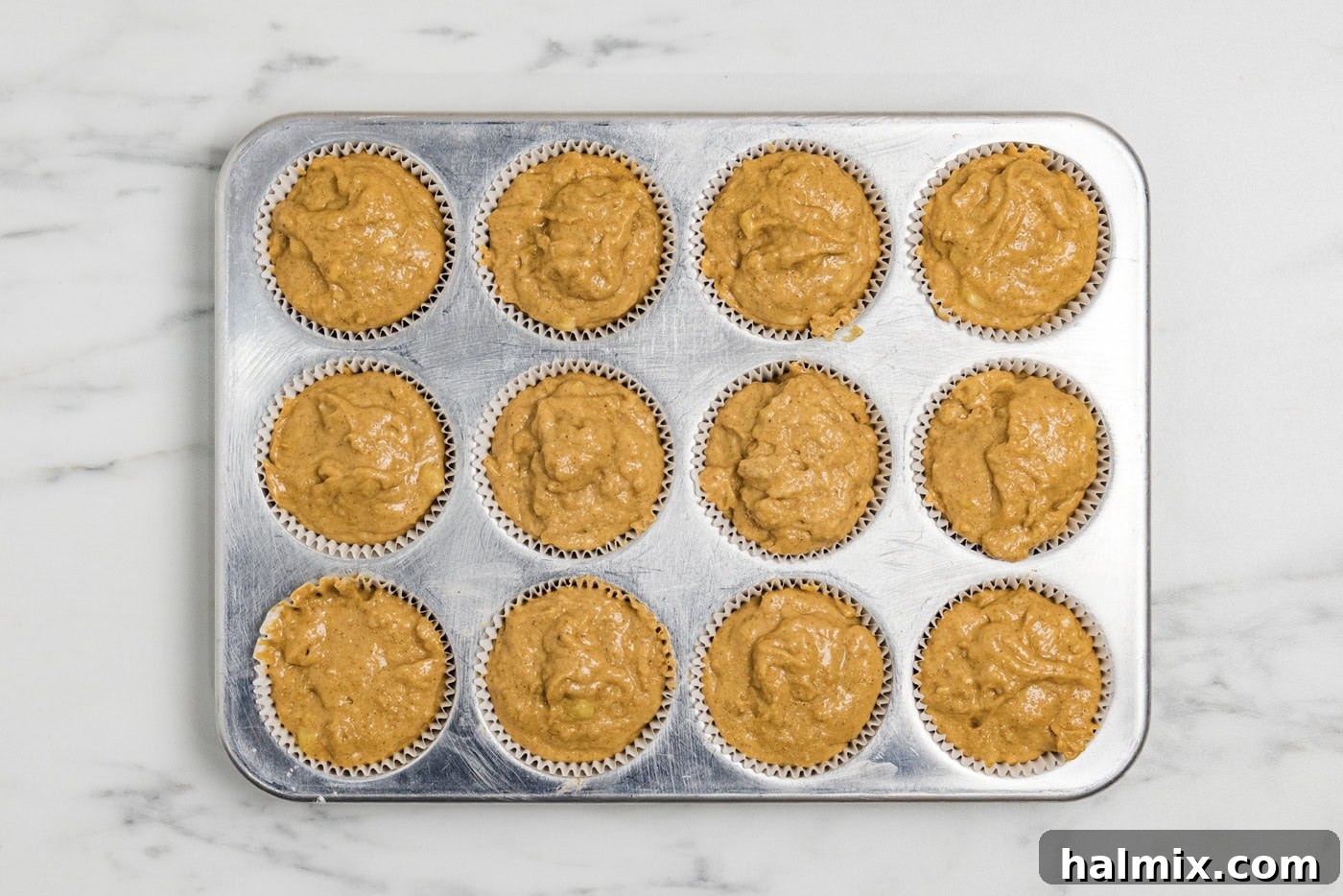 Pumpkin banana muffins batter in paper cups inside a muffin pan, ready for baking.