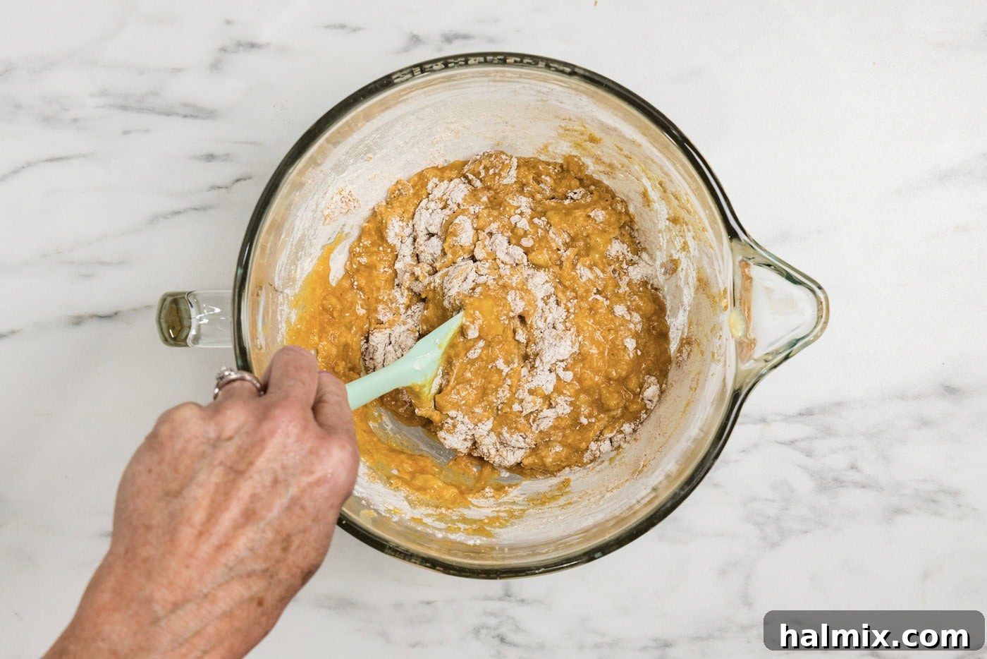 Hand using a rubber spatula to stir in dry ingredients into pumpkin mixture.