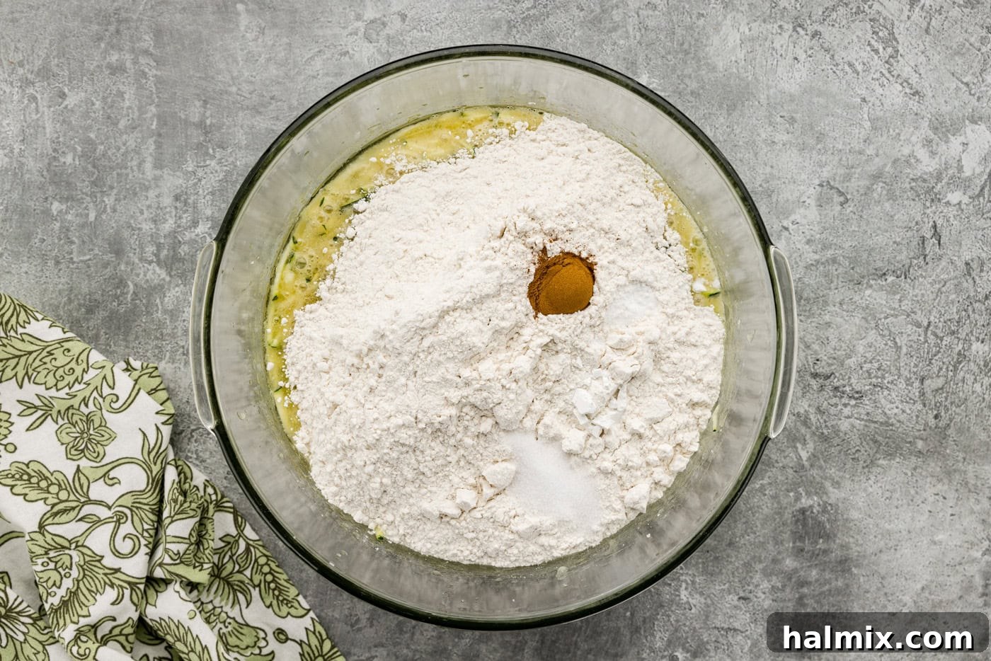 Dry ingredients added to zucchini mixture in a mixing bowl, ready to be mixed.