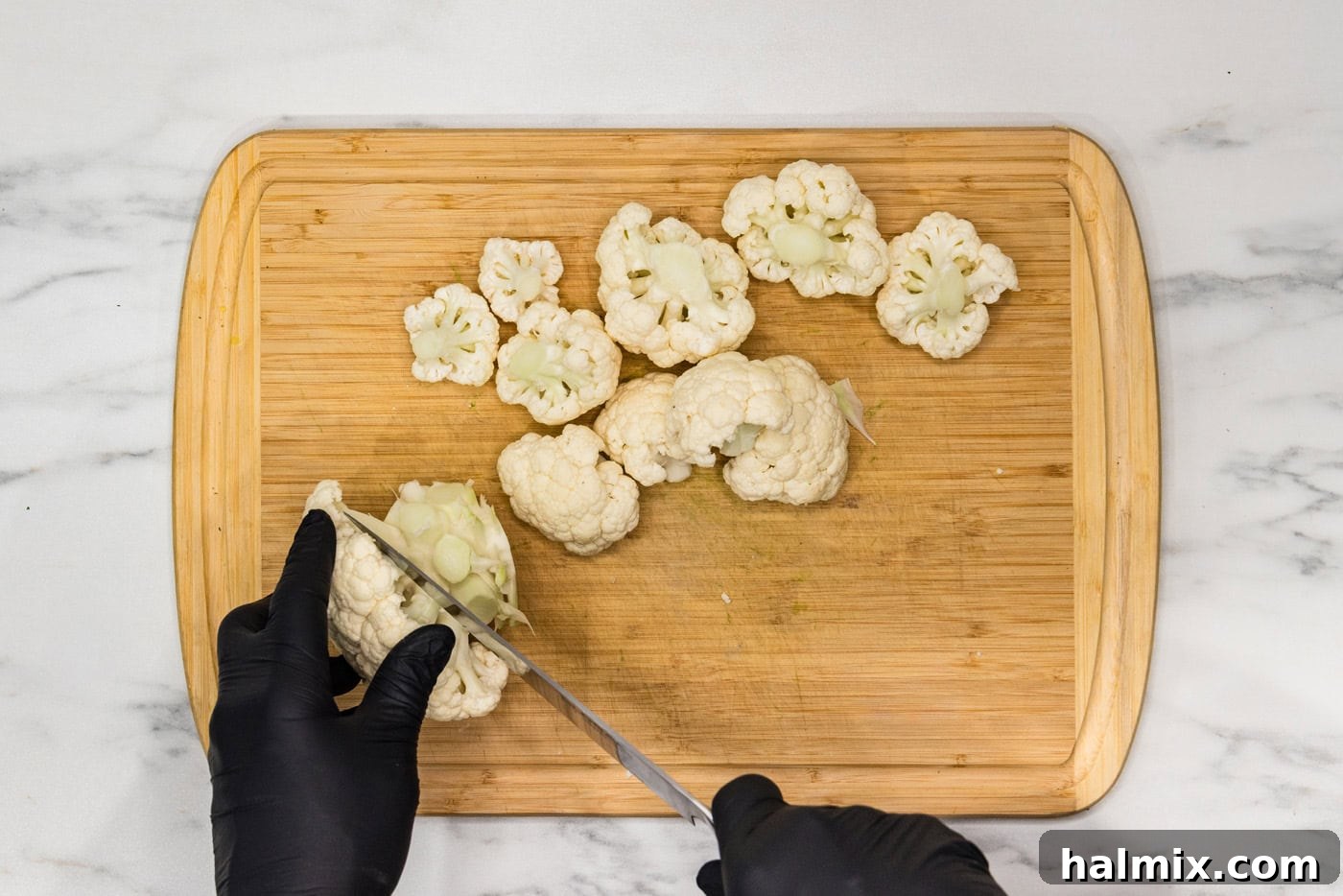 Perfectly Crispy Air Fryer Cauliflower 5 A hand using a knife on a cutting board to cut a cauliflower head into individual florets.