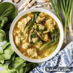 Bowl of Wonton Soup with green onions, mushrooms and baby bok choy around it, a delightful and vibrant presentation.