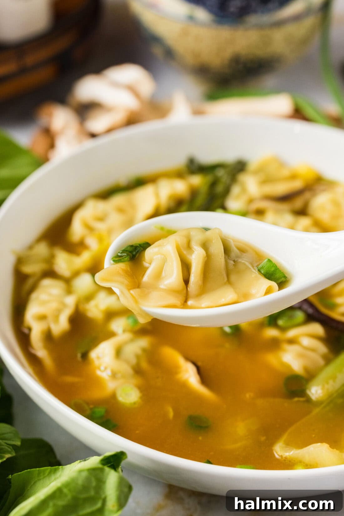 Close up photo of a wonton on a spoon held above a bowl of Wonton Soup, highlighting its perfect shape and appetizing texture.