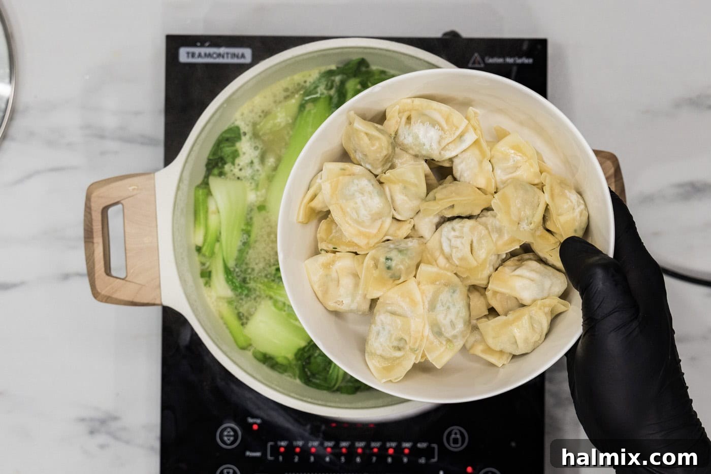 adding frozen wontons to stockpot with baby bok choy and chicken broth mixture, ready to plump up in the hot liquid.
