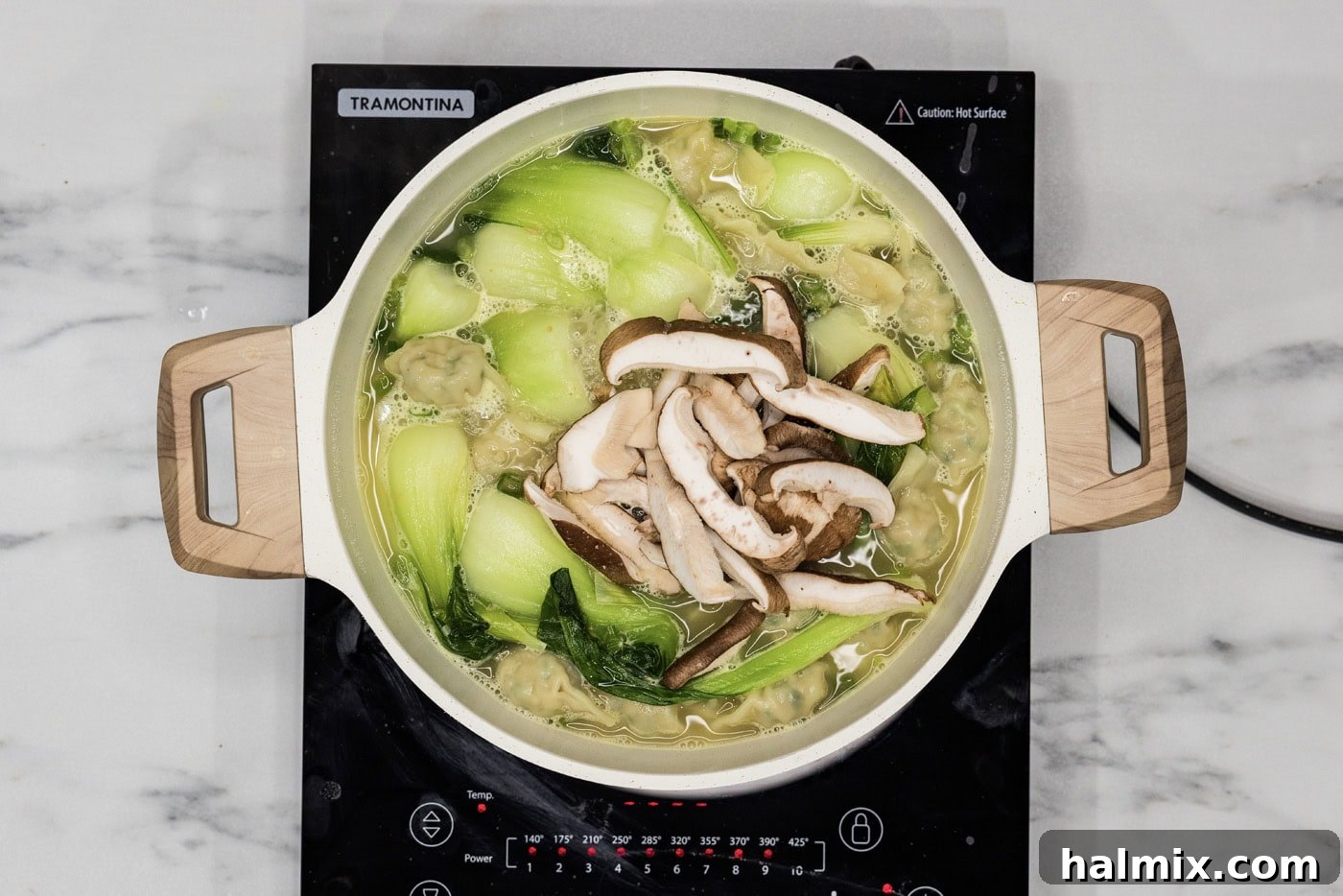 sliced shiitake mushrooms added to stockpot of wonton soup, contributing to its rich texture and umami.