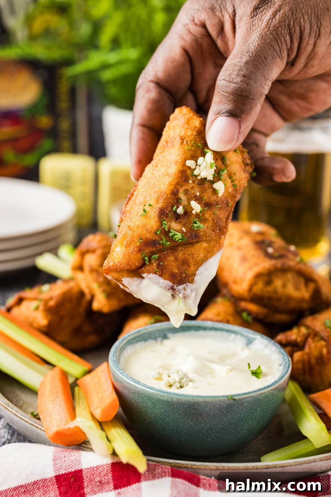 Hand holding a Buffalo Chicken Egg Roll dipped in blue cheese dressing