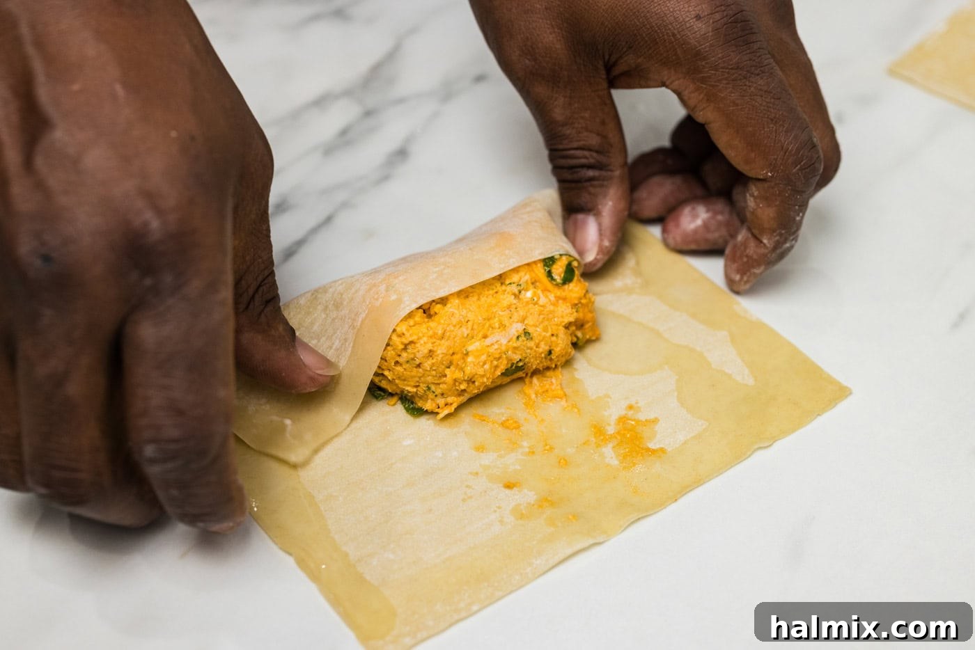 hands folding buffalo chicken mixture into egg rolls