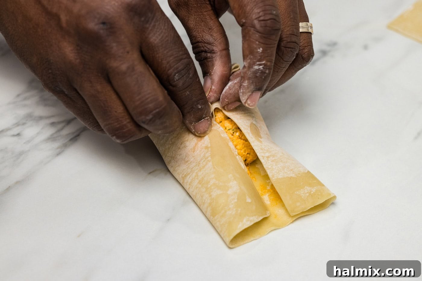 hands rolling egg roll wrapper over filling