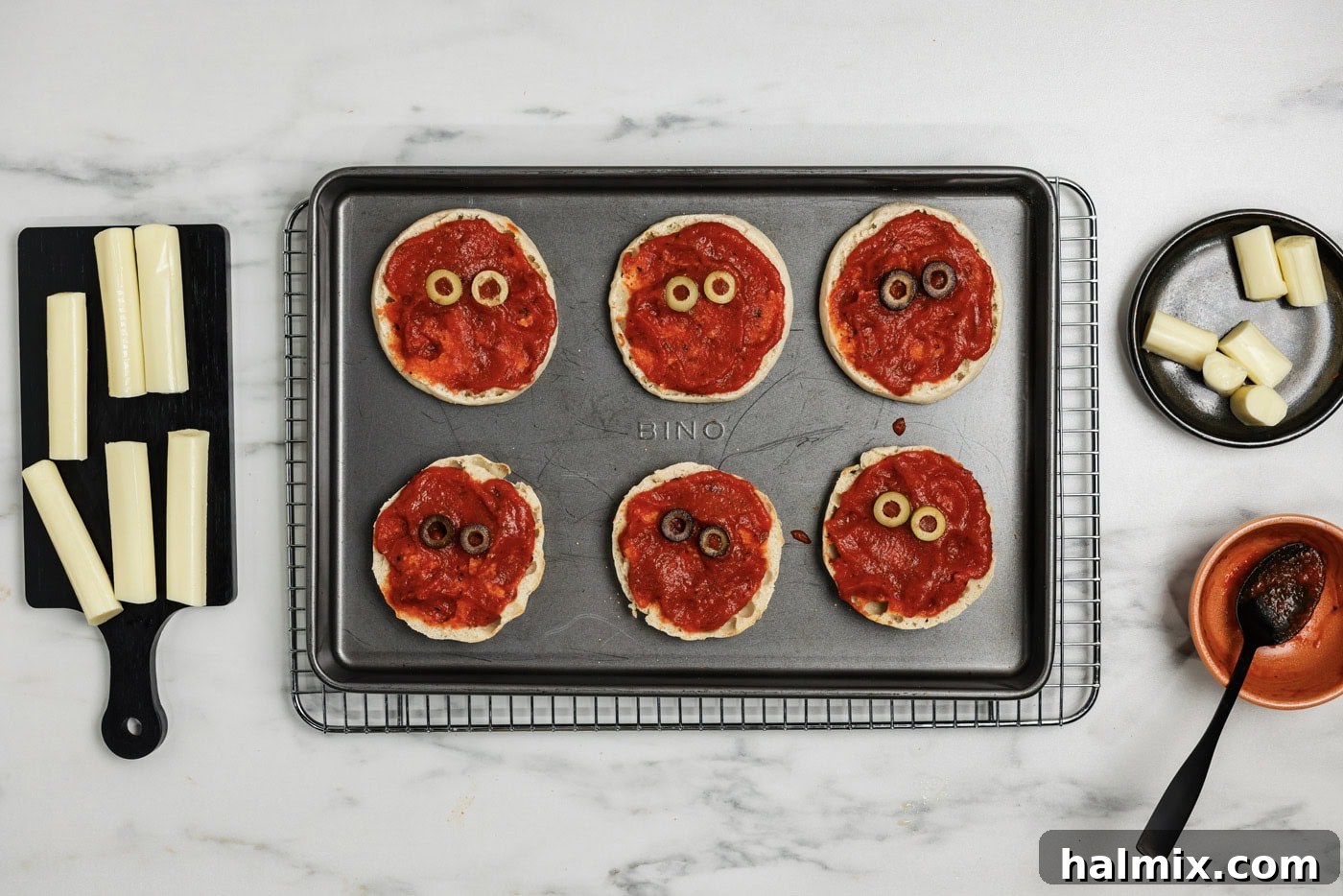 Sliced olives placed on top of sauced English muffins to look like eyes