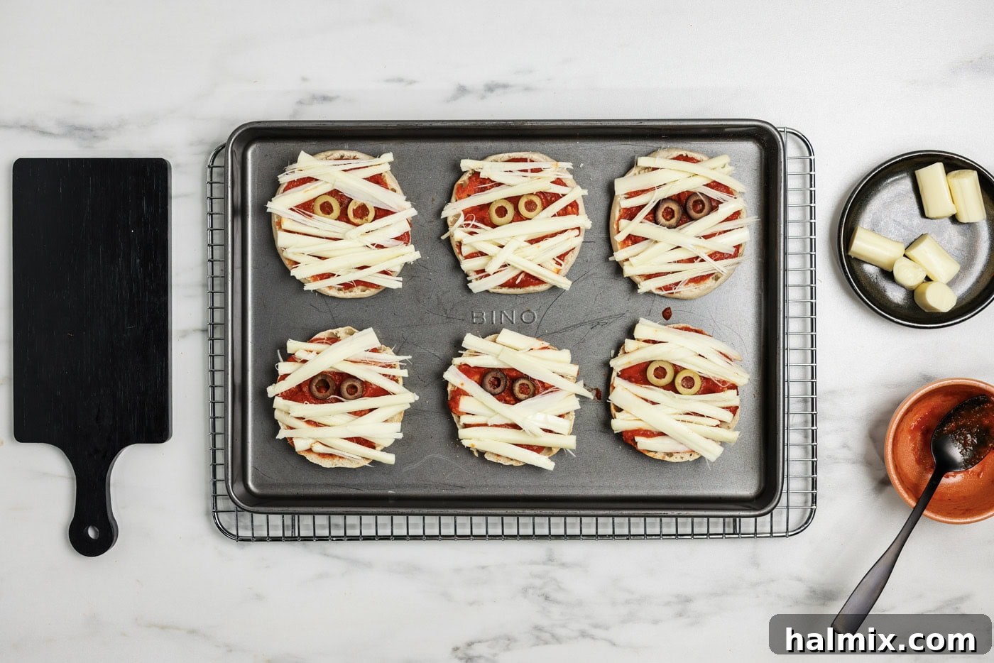 strips of cheese on top of English Muffins with sliced olive eyes to look like mummies