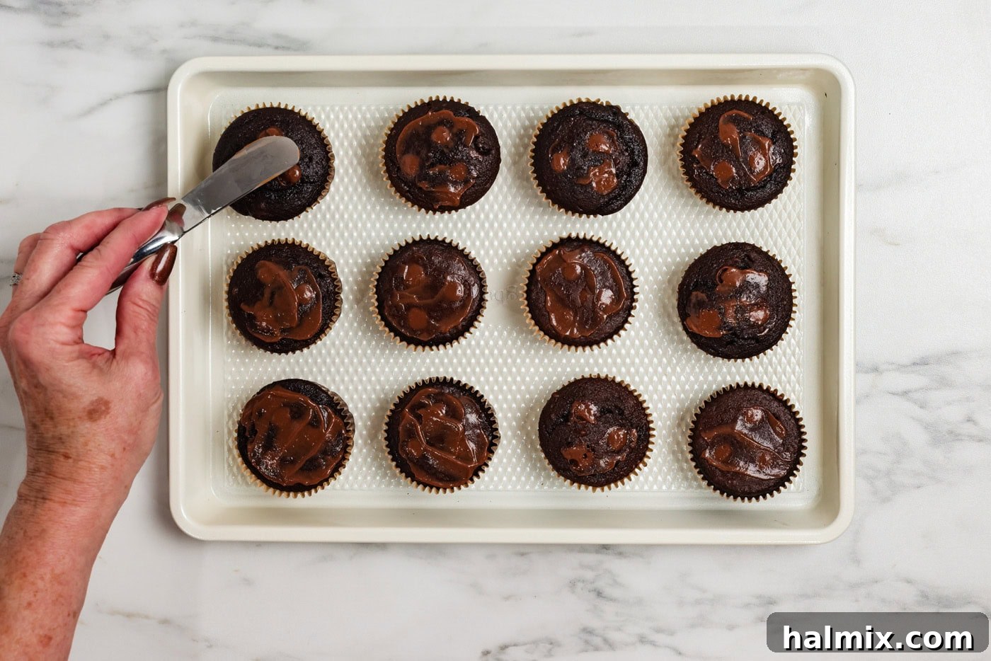 Using a small spatula to smear chocolate pudding over the cupcake holes