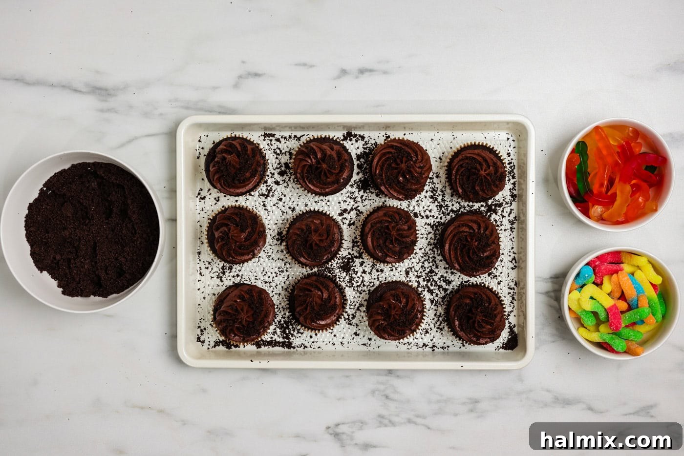 Crushed Oreos sprinkled over chocolate frosted cupcakes on a baking sheet