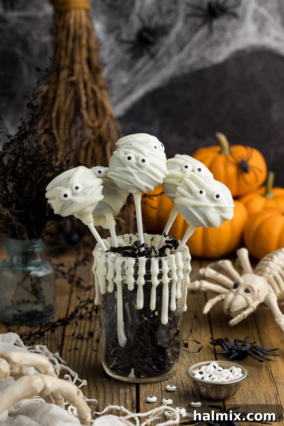 Delicious Mummy Pops resting in a decorative cup, showcasing their white chocolate 'bandages' and cute candy eyes against a dark background, perfect for Halloween.