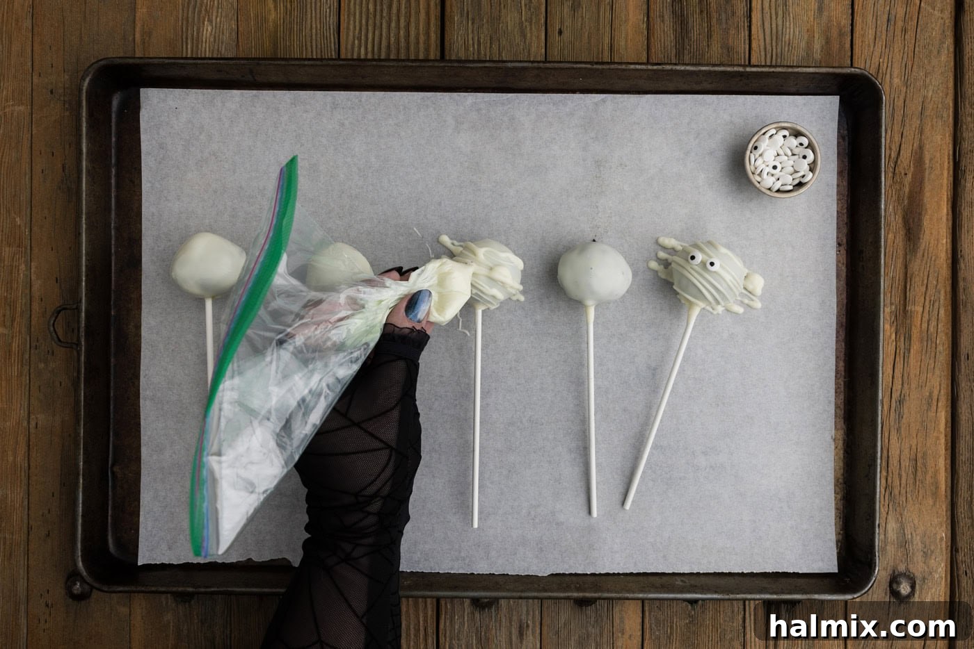 A close-up shot of drizzling melted white candy wafers over white chocolate coated Oreo truffles to create the mummy bandage effect, with candy eyes already placed.