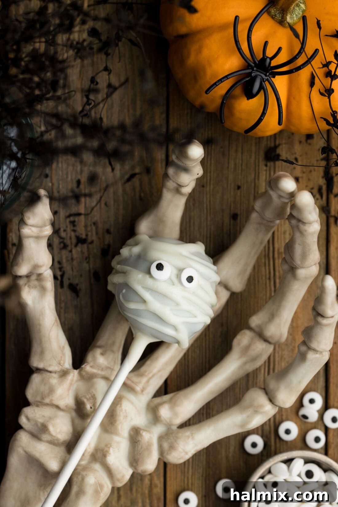 A festive Mummy Pop held by a skeletal hand, highlighting its spooky yet cute appearance, ready for Halloween festivities.