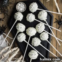 Mummy Pops resting in a coffin-shaped tray, adorned with white chocolate bandages and candy eyes, creating a festive Halloween dessert display.