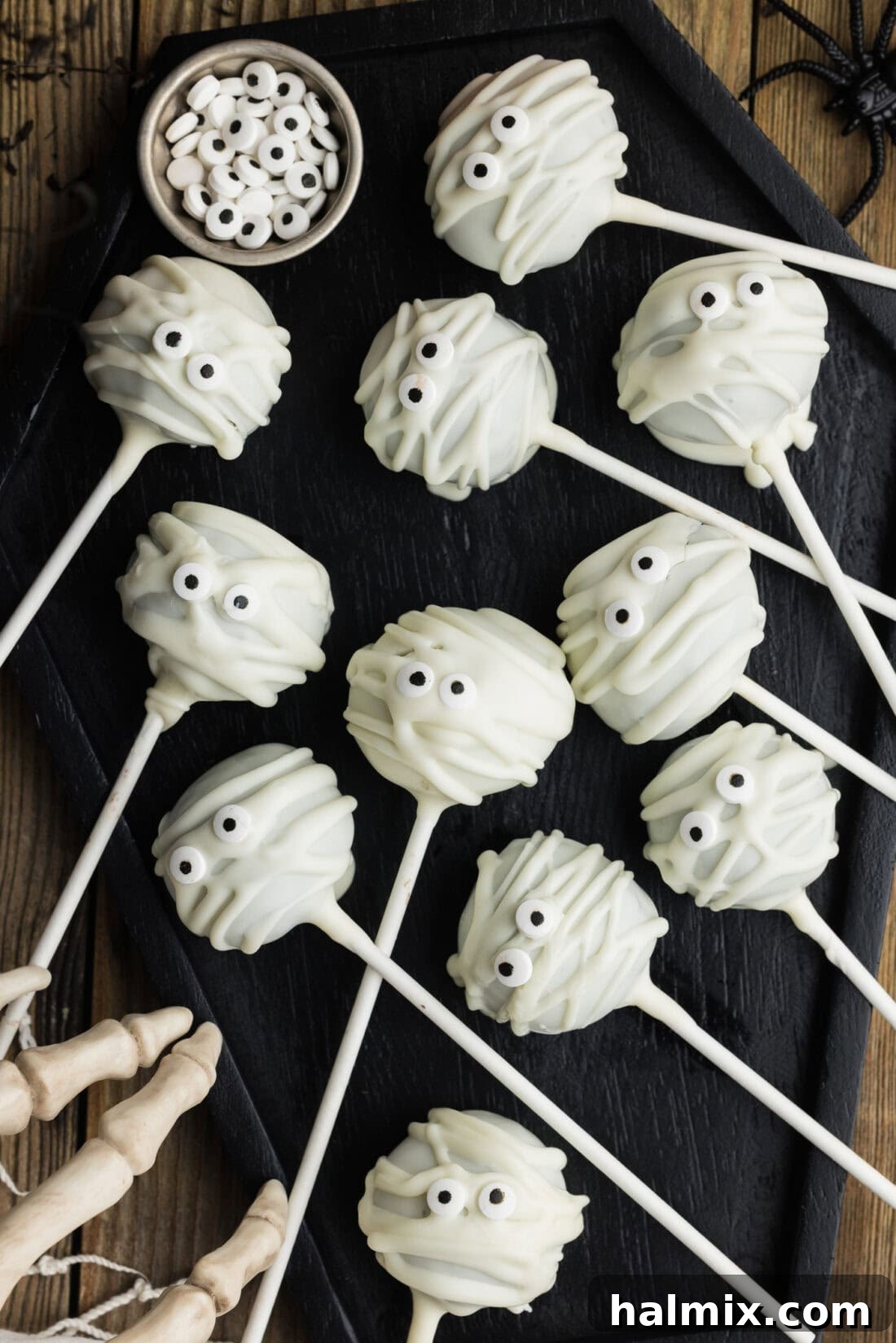 Close-up photo of multiple Mummy Pops arranged neatly in a black tray, showcasing their detailed white chocolate bandages and expressive candy eyes, ready for a Halloween party.