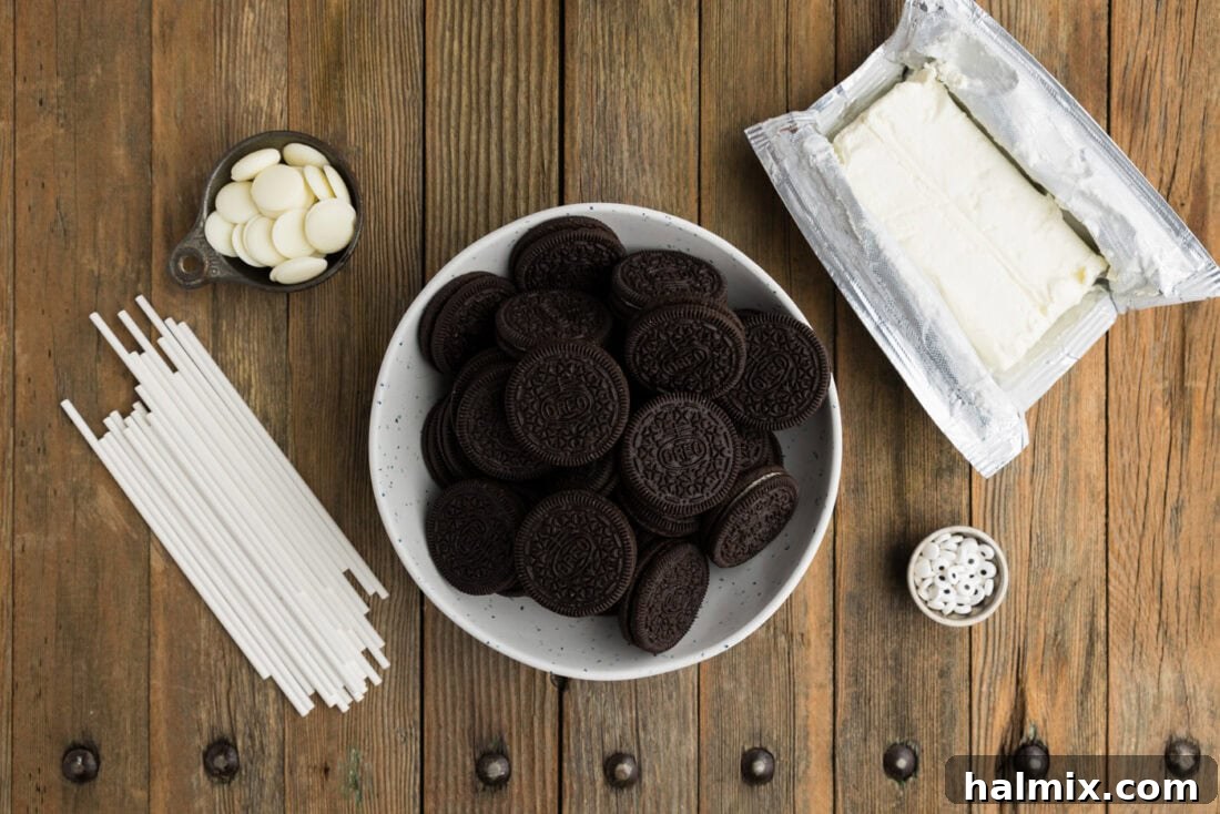 A flat lay of all the simple ingredients required to make Mummy Pops: Oreo cookies, a block of cream cheese, a bag of white melting wafers, and a container of candy eyeballs.