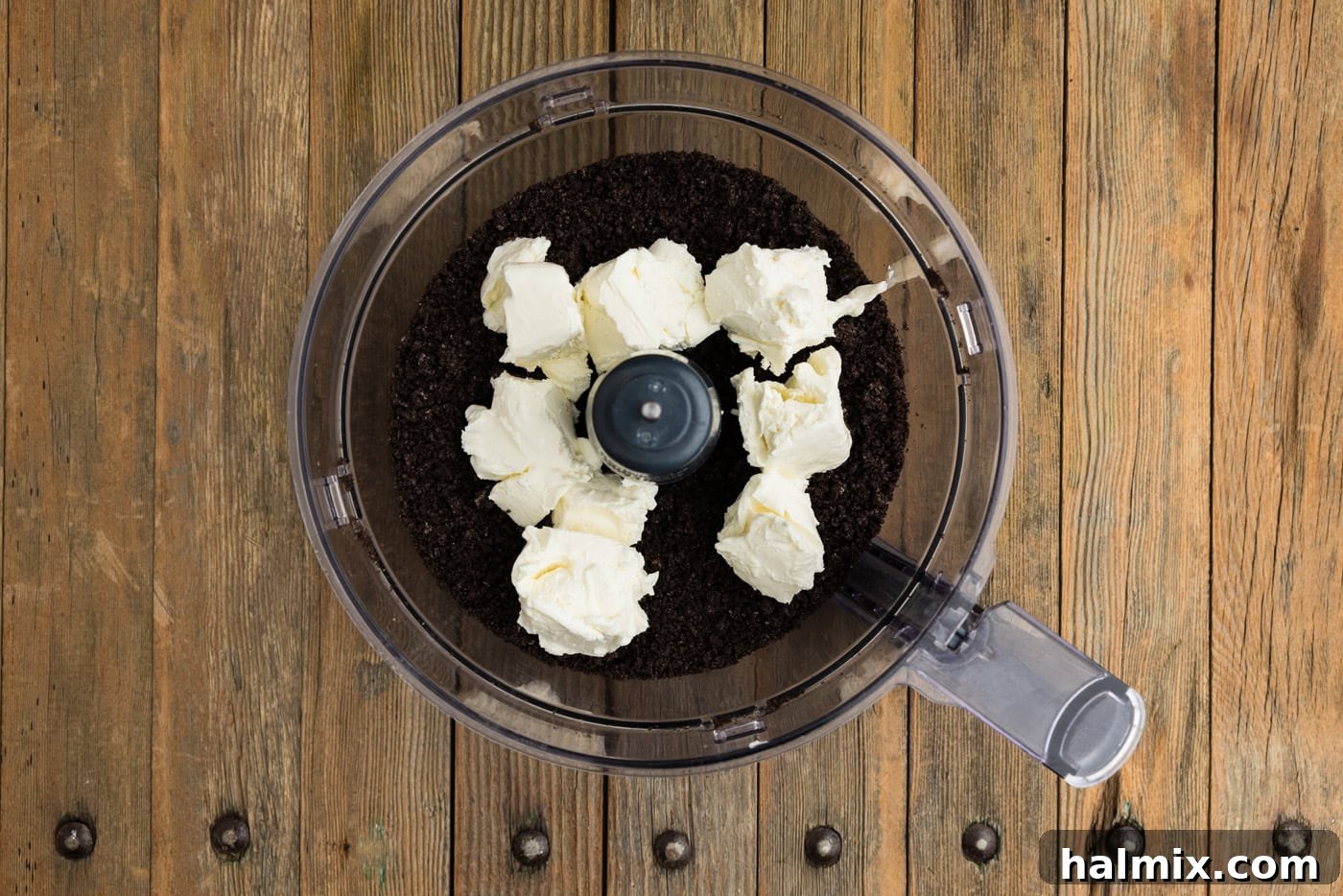 Cubed, softened cream cheese added to the bowl of a food processor with crushed Oreos, ready for blending.