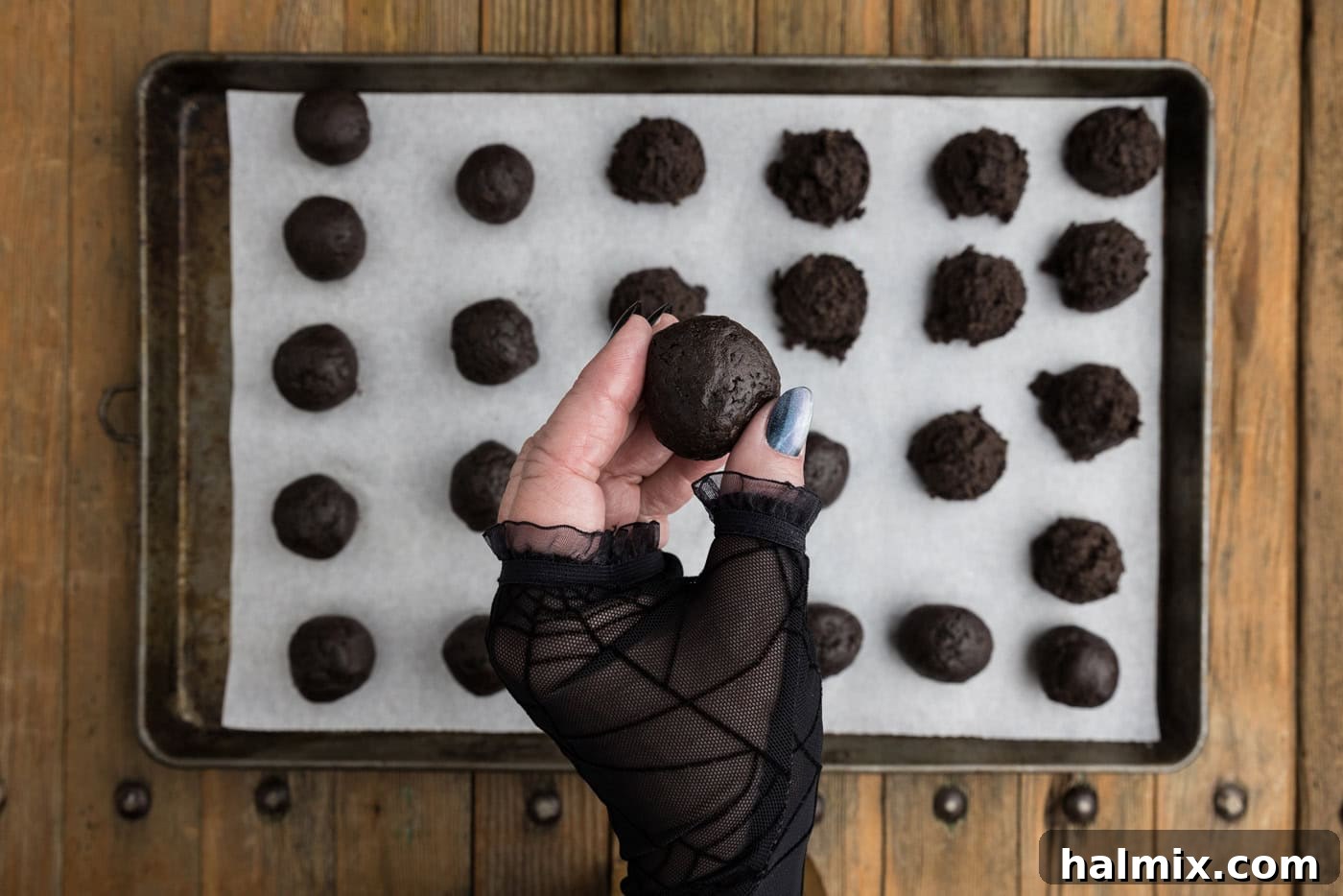 A hand gently rolling an Oreo truffle ball over a baking sheet, smoothing its surface before the next chilling phase.