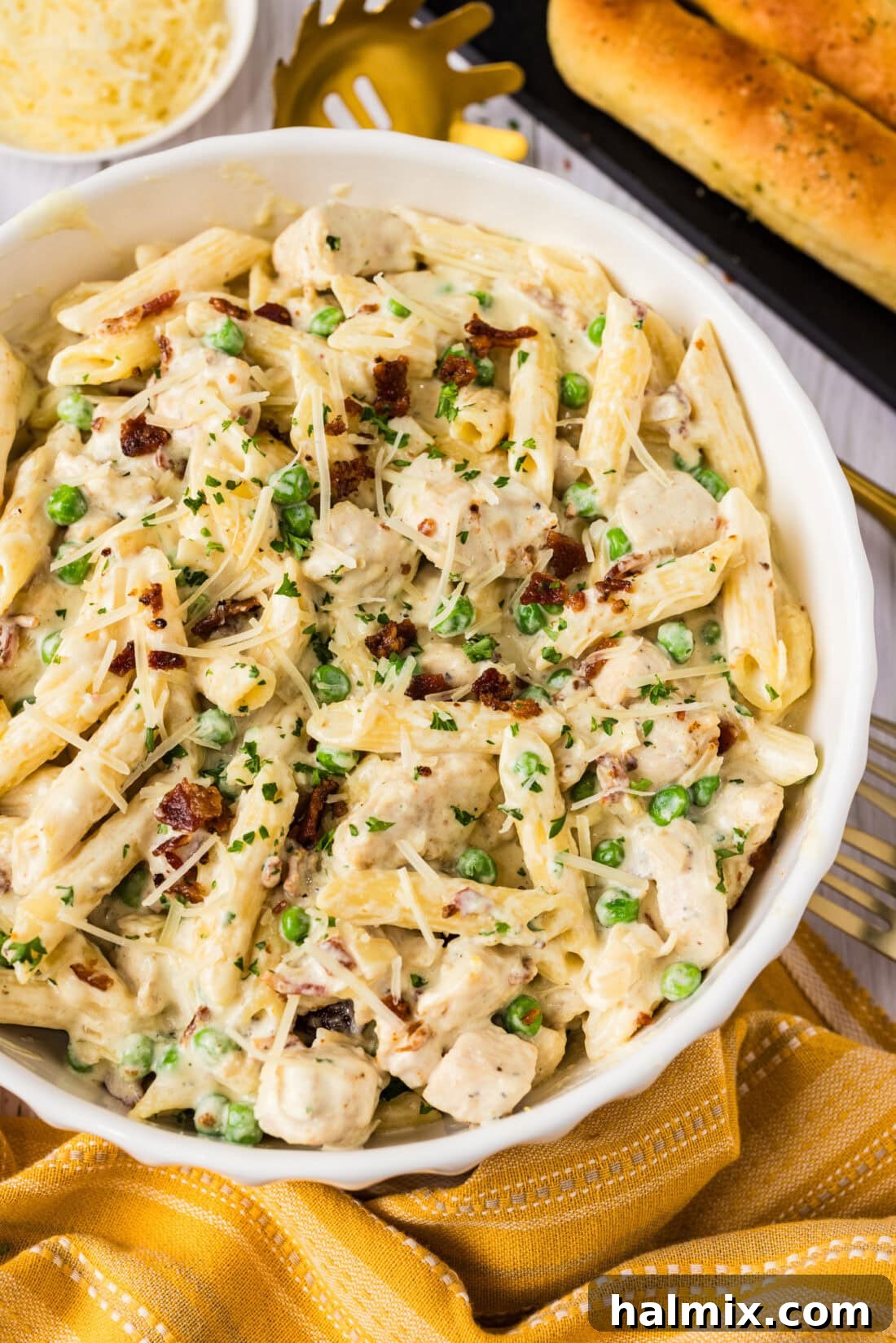 Close up photo of a bowl of Chicken Carbonara, highlighting the creamy sauce, chicken pieces, bacon, and peas.