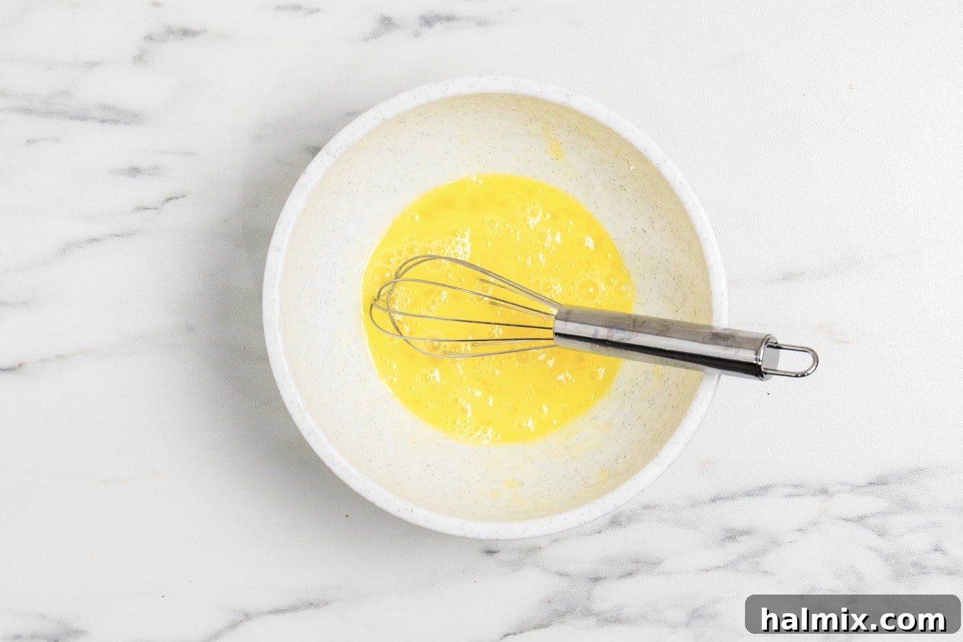 A medium bowl containing two whisked eggs, ready for tempering into the sauce.