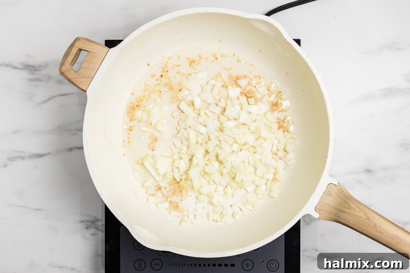 Chopped onion and minced garlic being sautéed in a hot skillet with olive oil, releasing their aromas.