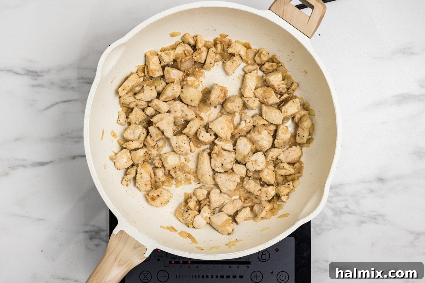 Cubed chicken pieces cooking in a skillet, turning golden brown as they cook through.