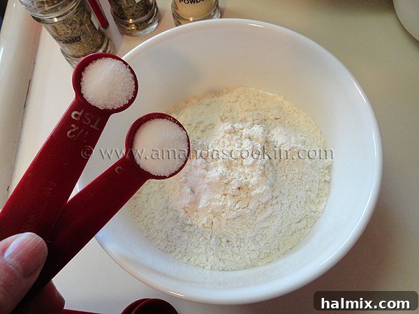 A close-up photo of salt being added to a bowl of all-purpose flour, ready to be mixed for the breading.