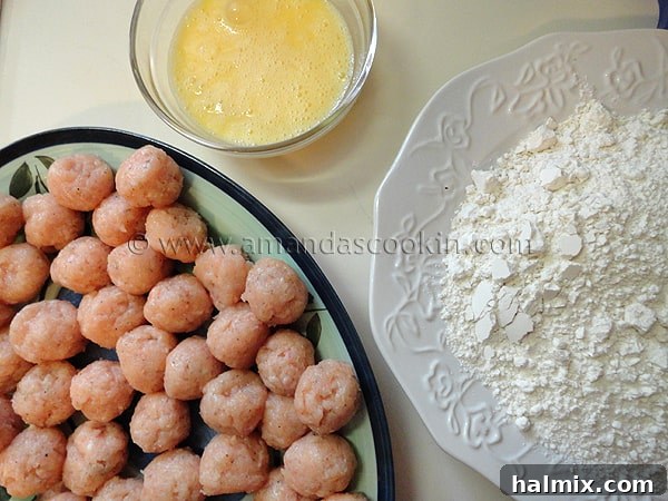 An organized breading station setup featuring a plate of raw chicken balls, a bowl of whisked eggs, and a plate of flour and salt mixture.