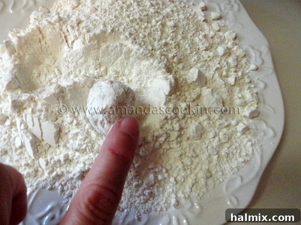 A hand gently rolling a chicken ball in a plate of flour, ensuring an even and complete coating.