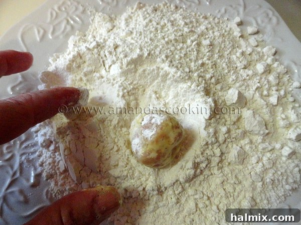 An egg-coated chicken ball being rolled back into the flour mixture for a second coating, creating a double-breaded effect.