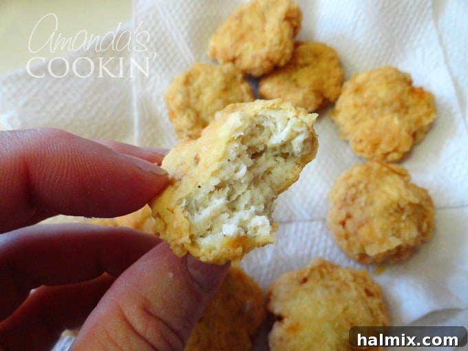 A mouth-watering close-up of a single homemade chicken nugget, showing its crispy breading and tender interior, inviting a bite.
