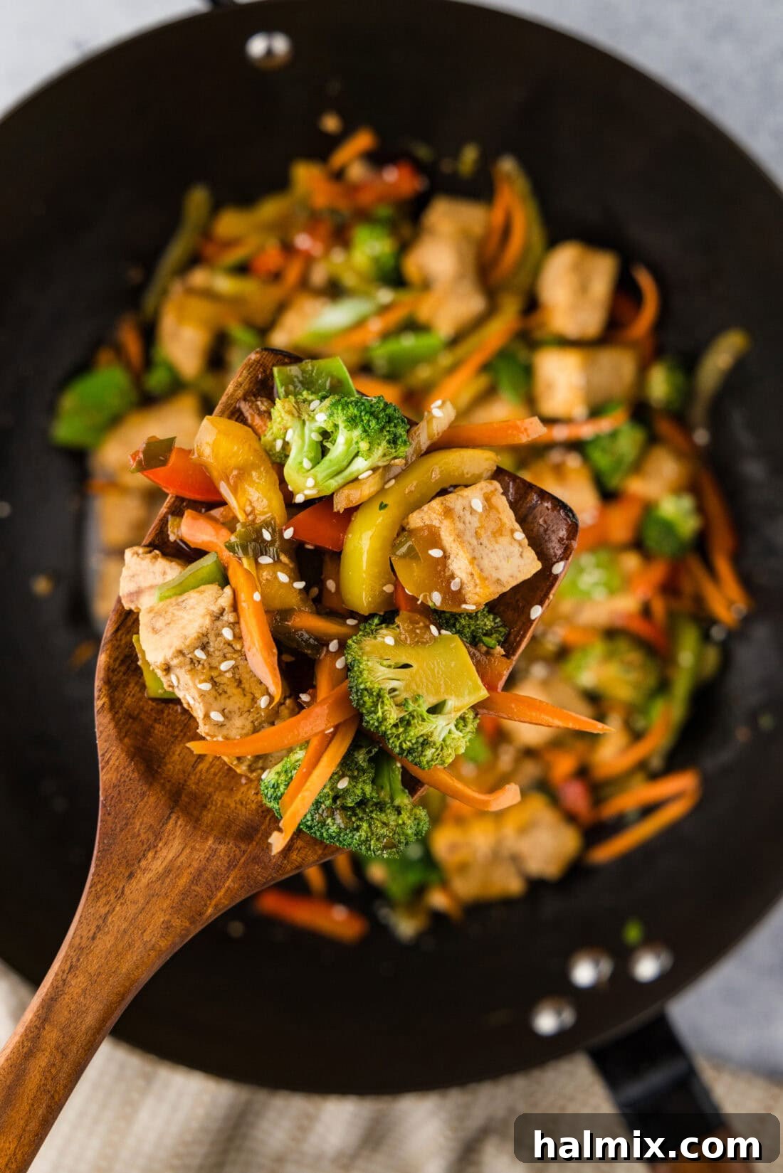Golden Tofu Stir-Fry 3 Spoonful of Tofu Stir Fry held above a wok of Tofu Stir Fry, showcasing the vibrant ingredients.