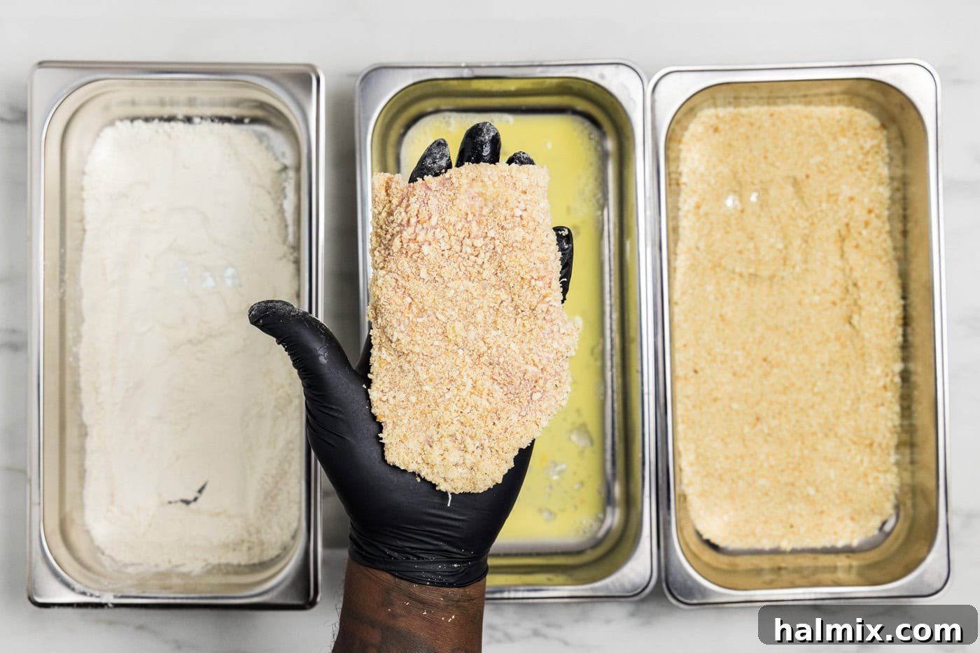 gloved hand holding panko breaded veal cutlet