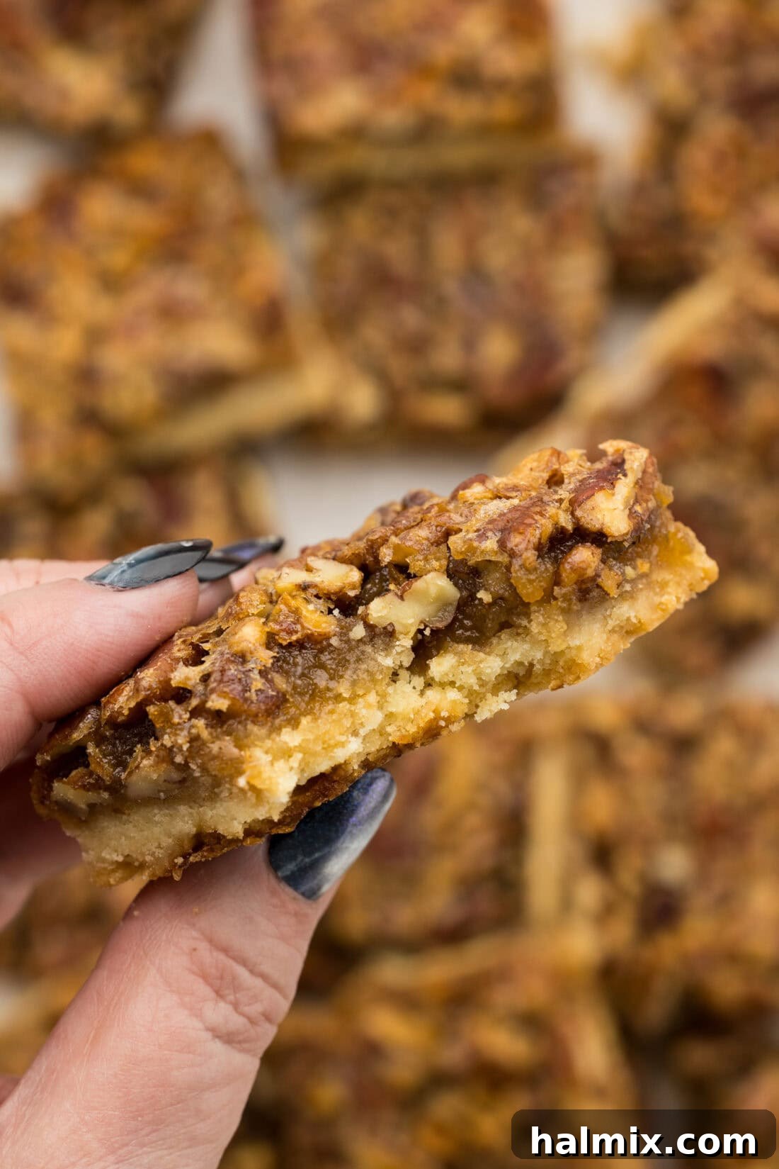 Decadent Pecan Pie Squares 11 A hand holding a perfectly sliced Pecan Pie Bar with a bite removed, showing the golden filling and pecan topping.