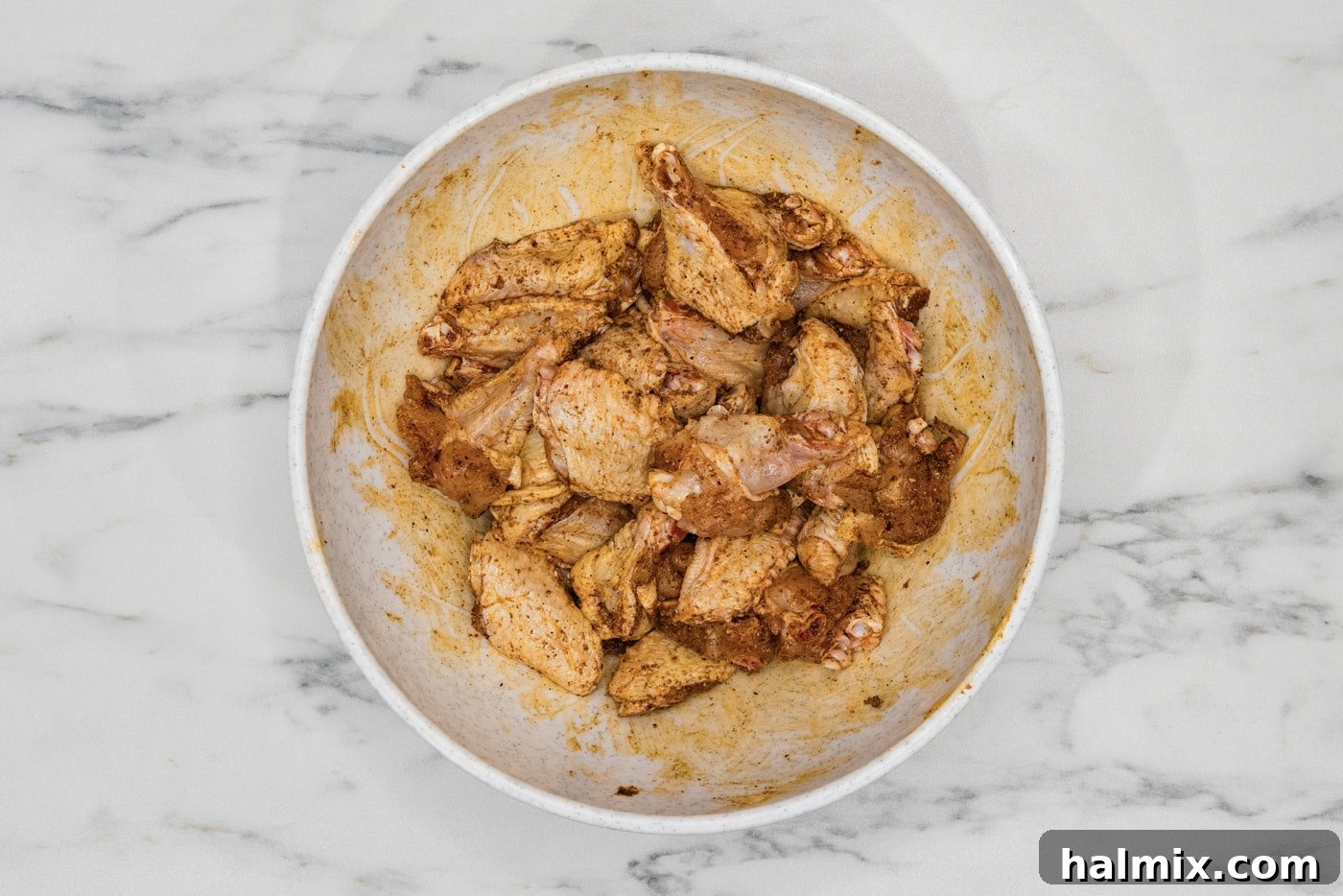 chicken wings in a bowl tossed in a rub