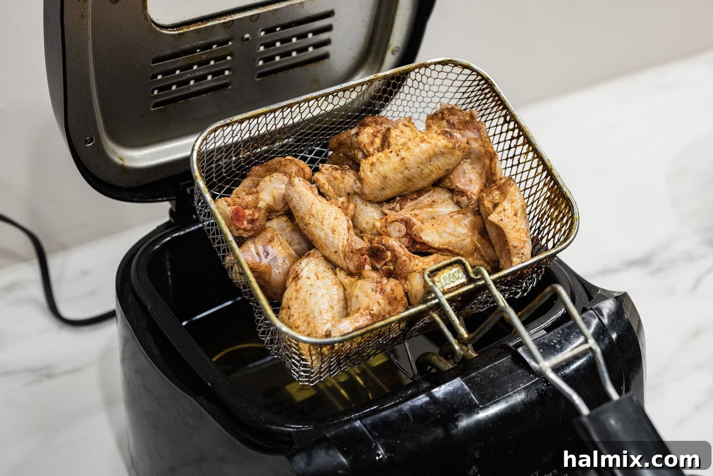 lowering basket of chicken wings into a deep fryer with oil