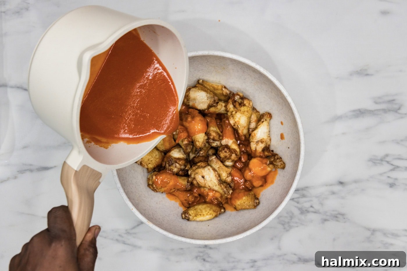 pouring buffalo sauce over chicken wings in a bowl