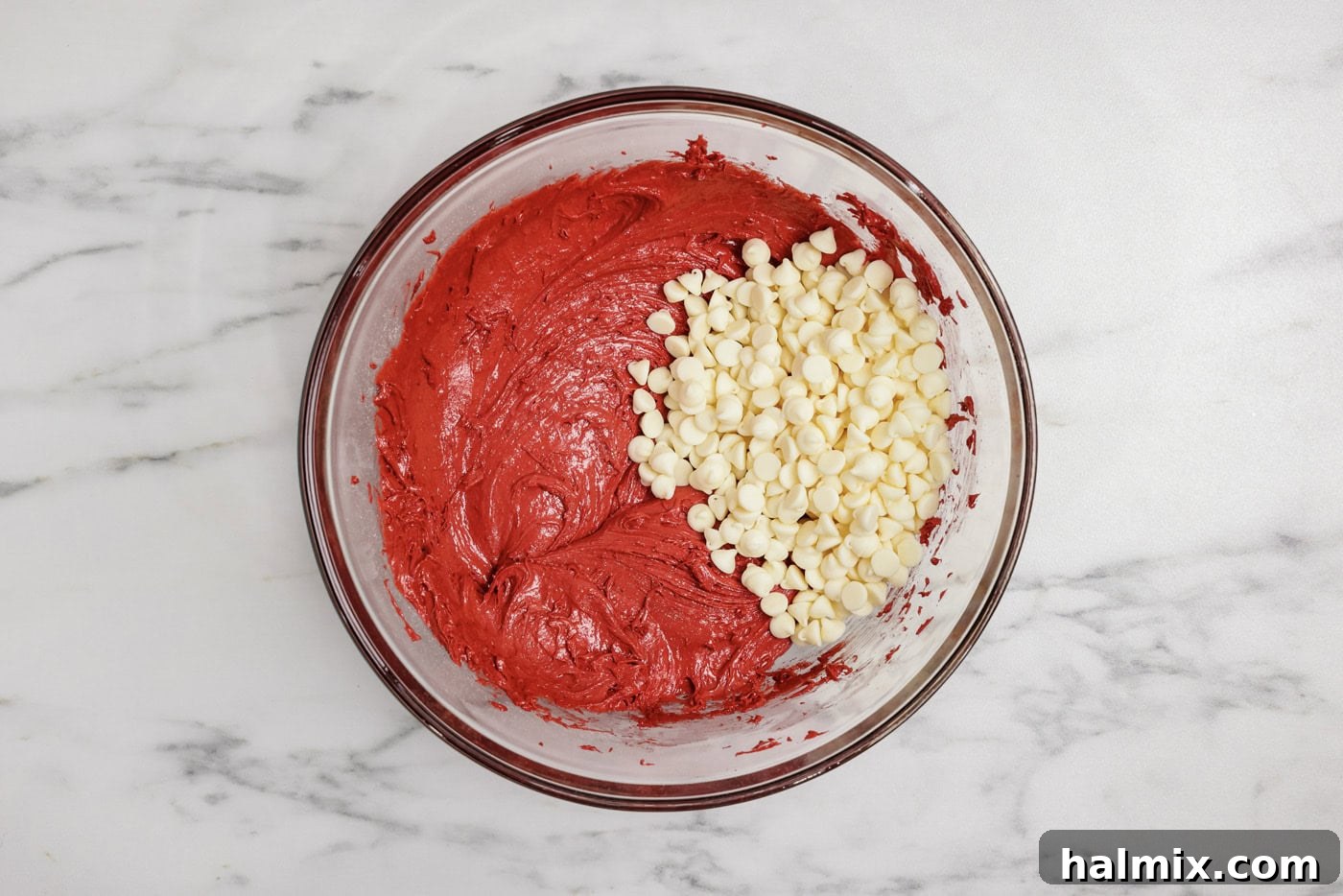 white chocolate chips added to red velvet cake batter in a mixing bowl