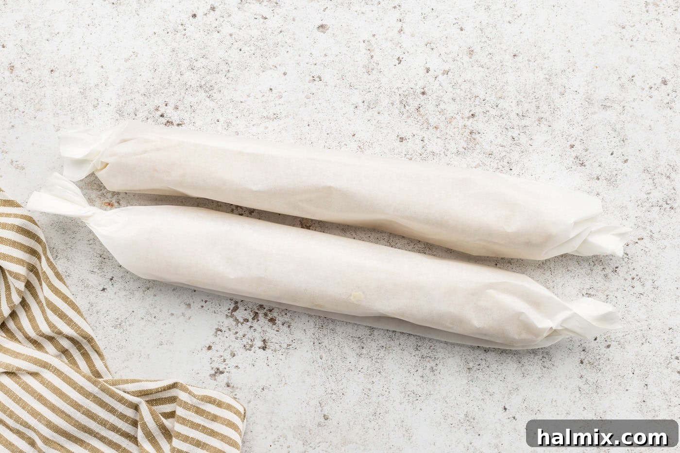 Two rolls of icebox cookie dough, neatly wrapped in parchment paper, ready for chilling.