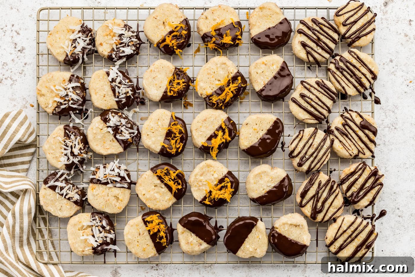 An overhead view of decorated icebox cookies, some with chocolate and garnishes, arranged on a wire cooling rack.
