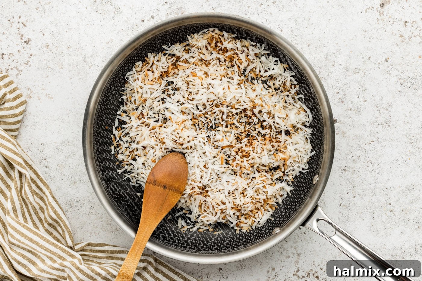 Toasted shredded coconut in a skillet with a wooden spoon, showing its golden-brown color.