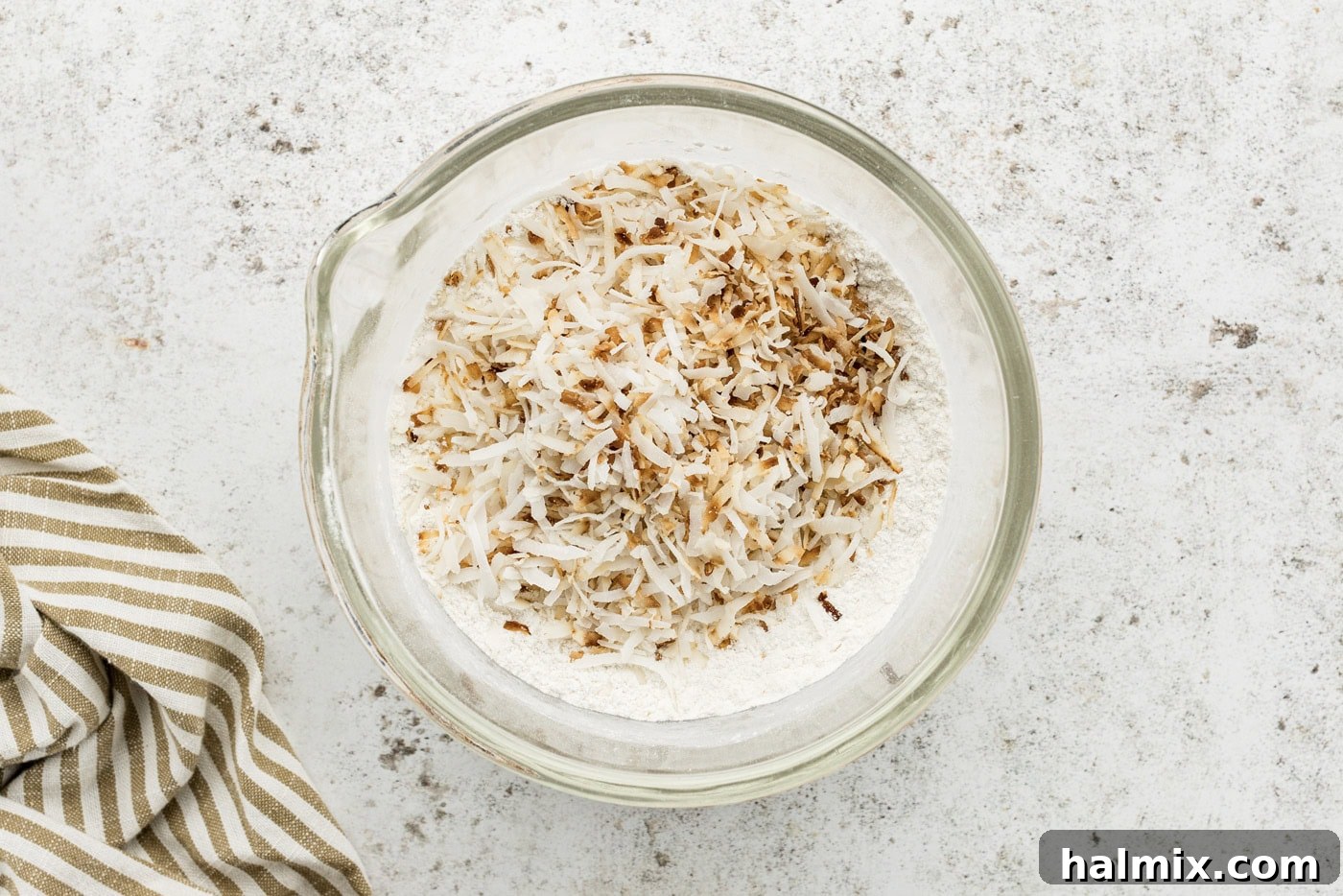 Toasted coconut flakes being added to a mixture of flour and salt in a large bowl.